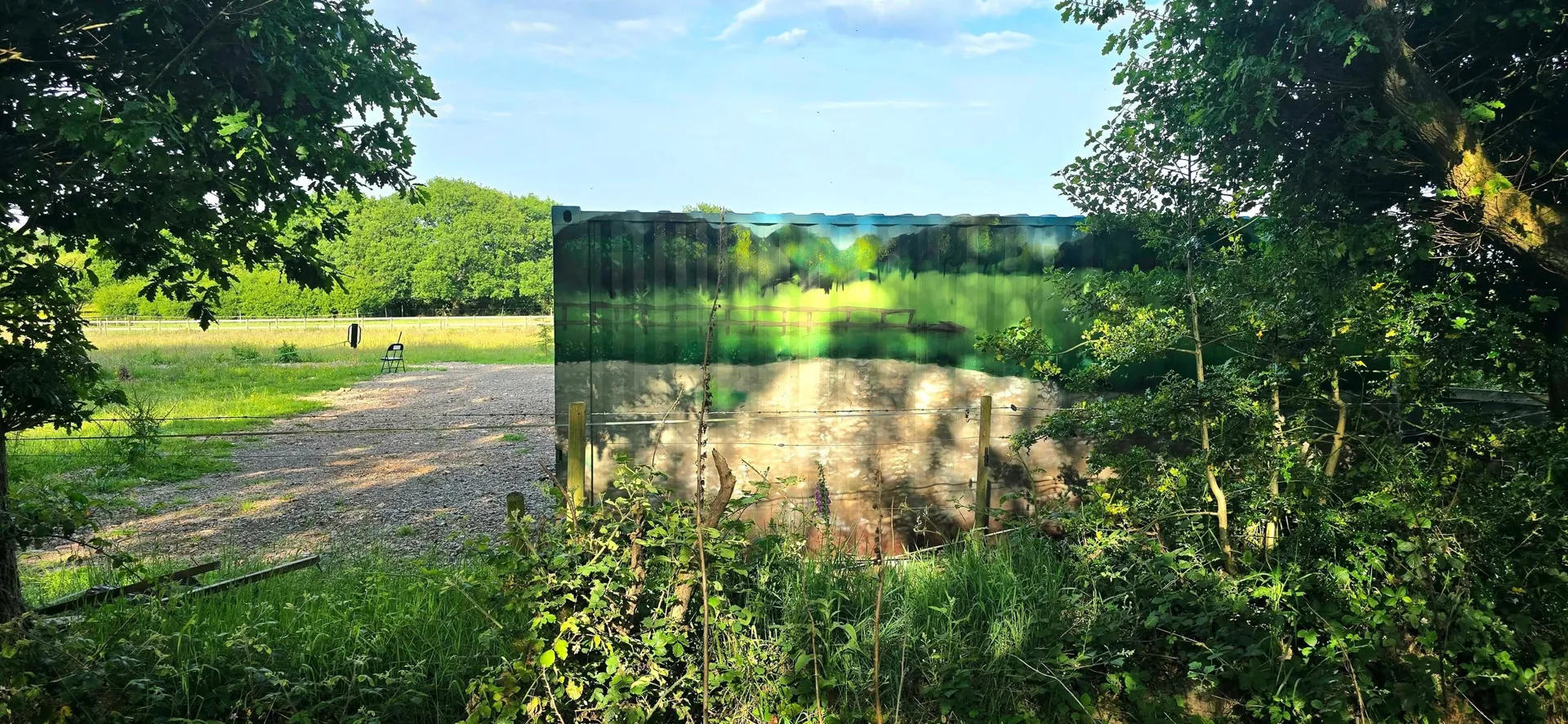 Shipping container wrapped in a printed landscape so it blends into the surrounding field