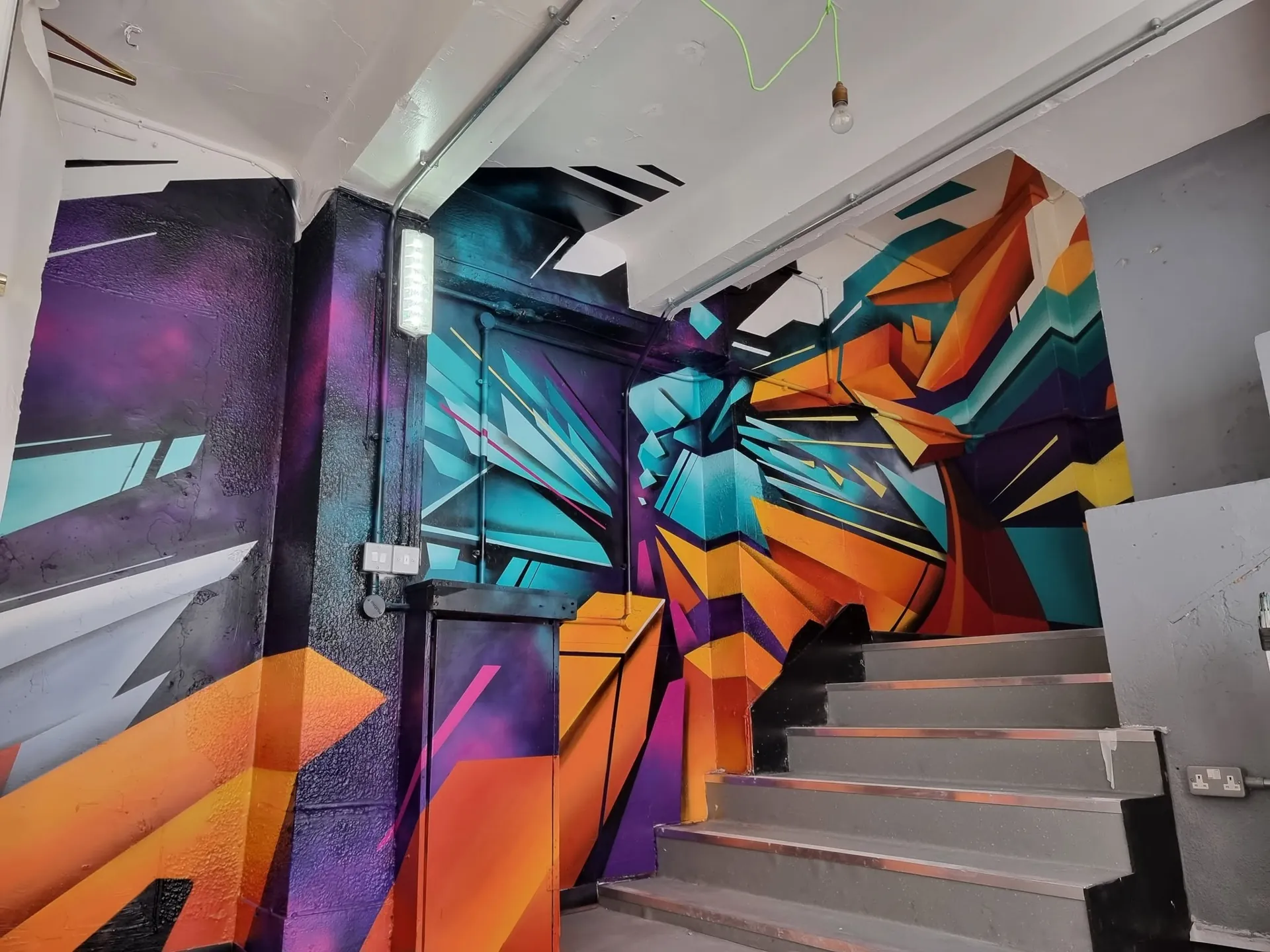 Bold graffiti-style feature wall running up an office stairwell in orange, teal and purple