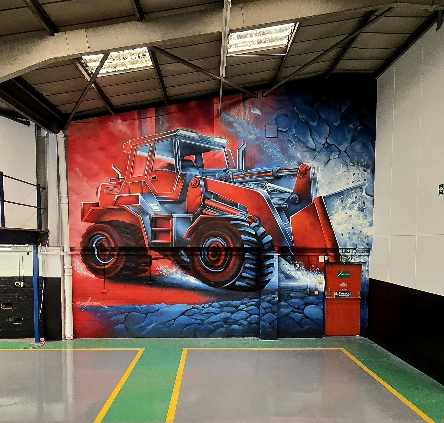 Large mural of a red wheel loader on the back wall of an industrial unit